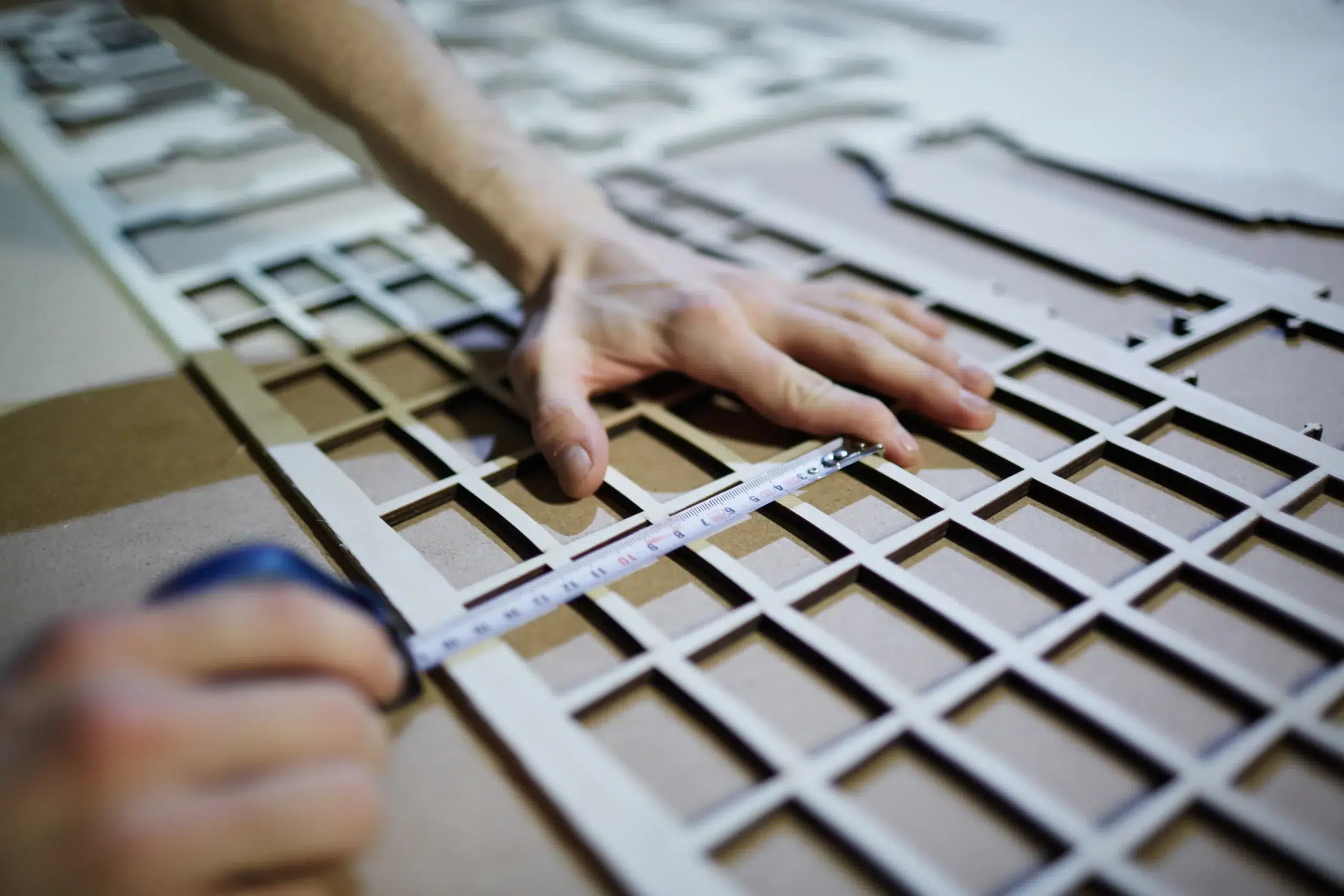 Person measuring a window frame with a tape measure and cutting tool, detailing grid-like framework for shutters. how to measure your windows for shutters guide.